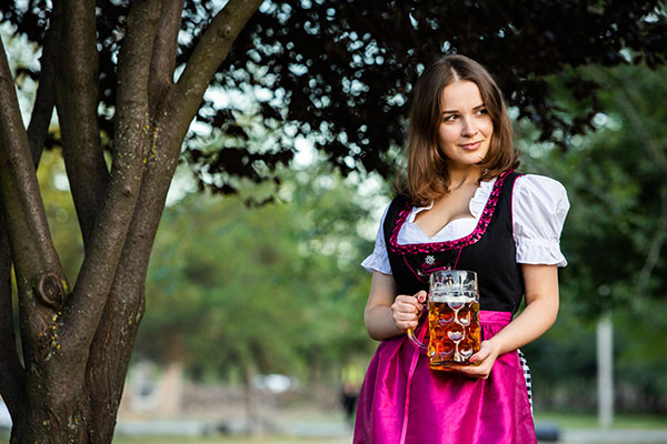 Junge Frau in schönem Dirndl mit Bierkrug unter einem Baum